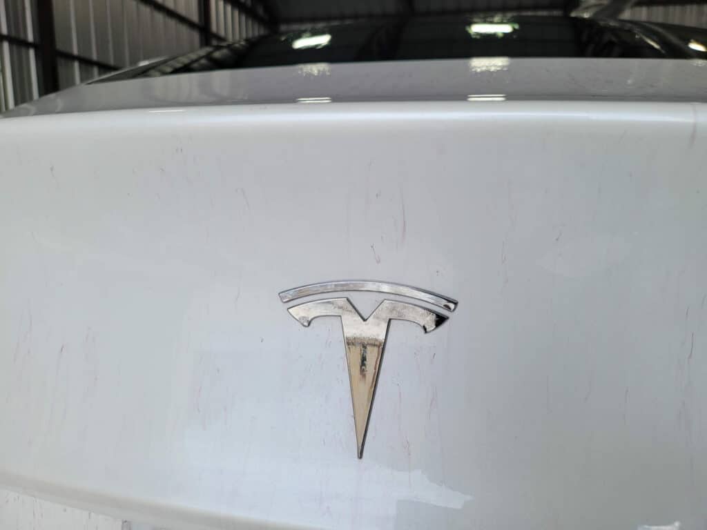 White tesla boot and logo with CarPro iron x fallout remover applied. You can see the purple lines left as the iron is dissolved.